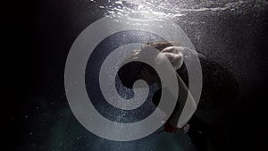 female figure in dark depth underwater, woman is floating in water of sea or ocean