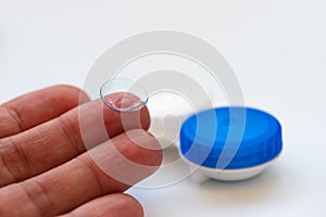 Female finger with contact lens and contact lens case on white background. Soft focus. Macro. Opthalmology and health concept