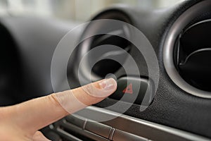 Female finger hitting emergency light stop button in the car, woman pressing red triangle car hazard warning button.