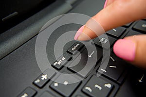 Female finger presses delete button on black laptop
