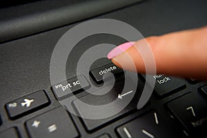 Female finger presses delete button on black laptop