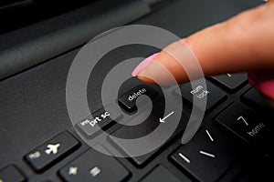 Female finger presses delete button on black laptop