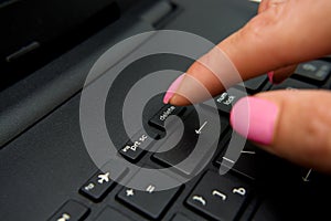 Female finger presses delete button on black laptop