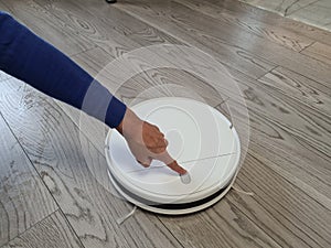Female finger pressing power button on white robotic vacuum cleaner
