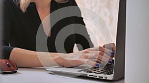 Female fingers with blue nail polish entering data on computer