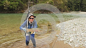 Female fisherman holding a large brown trout at a river in new zealand