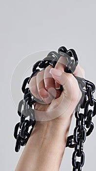Female fist holding metal chain high up over grey background