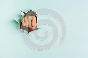 Female fist punching through blue paper background. War, struggle, conflict, feminist concept. Banner with copy space photo