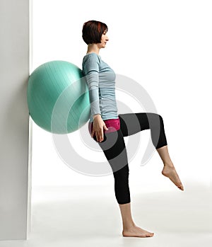 Female fitness instructor holds legs in gym and workout exercises for abdominals with green sport ball over white