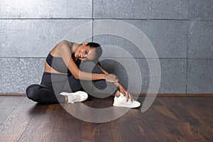 Female fitness instructor sitting on the floor with her head resting on her leg in fitness outfit