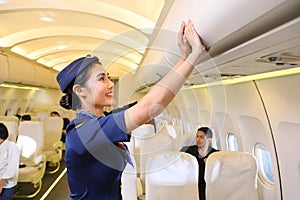 Female flight attendant closing the overhead luggage compartment lid after all passengers are seated photo