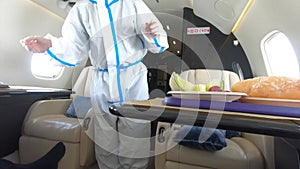 Female flight attendant  in full protective clothing is serving delicious food and hot drink inside a luxury private jet