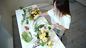 Female floral technician engaged in arranging flowers for event in office in daytime.