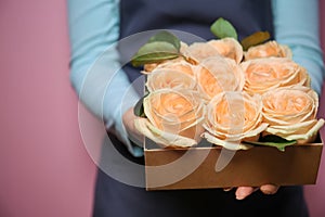 Female florist holding gift box with beautiful roses on color background, closeup