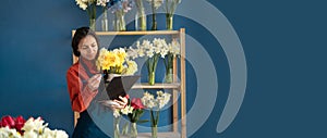 A female florist holds a bouquet and makes notes on a clipboard while standing in her flower shop. Small business and