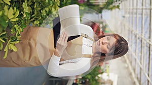 Female florist standing, working in greenhouse, inspecting plants.