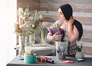 Female florist at work: pretty young dark-haired woman making fashion modern bouquet of different flowers. Women working