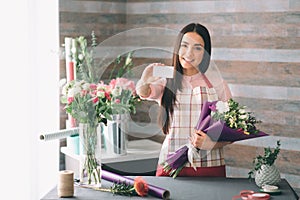 Female florist at work: pretty young dark-haired woman making fashion modern bouquet of different flowers. Women working