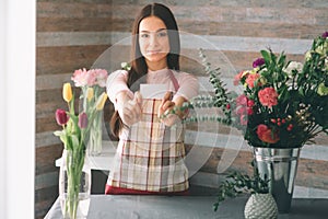 Female florist at work: pretty young dark-haired woman making fashion modern bouquet of different flowers. Women working