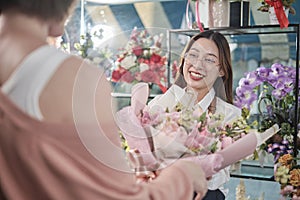 Female florist worker delivers fresh floras to customer in flower shop.