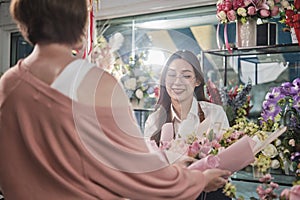 Female florist worker delivers fresh floras to customer in flower shop.