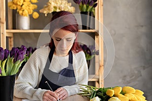 A female flower business owner wrote down an order for a bouquet of flowers in a notebook. European flower shop concept.