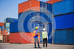 Female foreman with safety vest holding laptop and  worker man in hardhat checking and control loading containers box from cargo