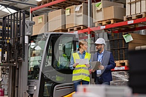 Female forklift driver talking with manager in warehouse, order picking. Warehouse worker preparing products for