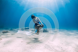 Female free diver with fins posing underwater in sea with sunlight