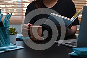 Female freelancer drinking coffee and reading book at home