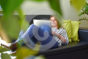 Female freelancer lies on a sofa in a room with a computer