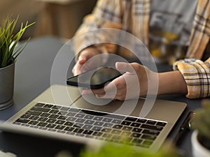 Female freelancer working smartphone and laptop on simple workspace in home office room