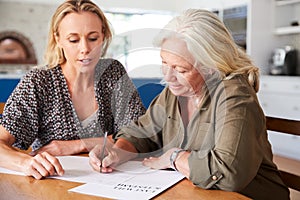 Female Friend Helping Senior Woman To Complete Last Will And Testament At Home