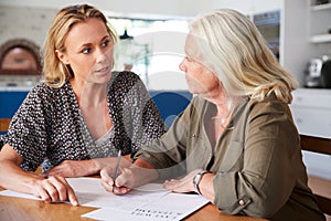 Female Friend Helping Senior Woman To Complete Last Will And Testament At Home