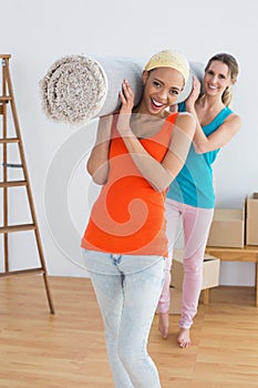 Female friends carrying rolled rug after moving in a house