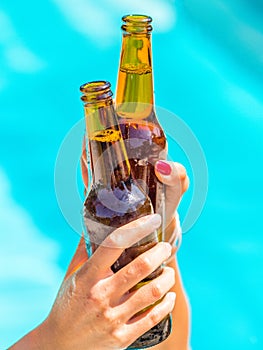 Female friends cheer clinking bottles of beer in their hands next to a pool of blue water