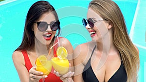 Female friends clinking cocktails at pool party, enjoying vacation luxury resort