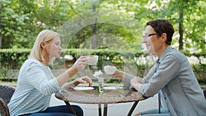 Female friends clinking coffee cups talking celebrating meeting in street cafe