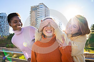 Female friends covering each other eyes for a surprise. Girls having fun together laughing.