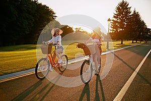 Female friends cycling together along local road at sunset