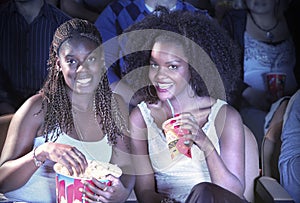 Female Friends With Drink And Popcorn Watching Movie In Theater