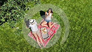 Female friends eating pizza on summer picnic in park, relaxing on grass and having fun, aerial drone view