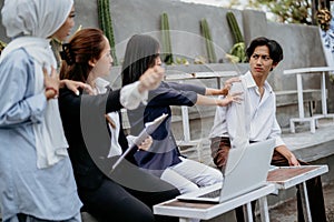 female friends encourage a male friend to use a laptop while sitting