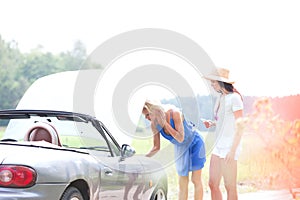 Female friends examining broken down car on country road