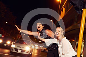 Female friends hailing taxi on city street at night photo
