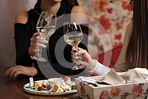 Female friends - hands clinking white wine glasses, restaurant or bar on background, close up view. evening, celebration