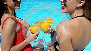 Female friends having fun at poolside and drinking cocktails, summer pool party