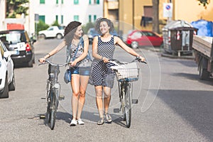 Female friends holding bikes and walking in the city