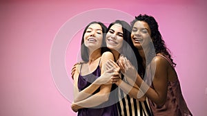 Female friends hugging and posing for camera on pink background, pajama party