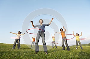 Female Friends Playing With Hula Hoop Against Sky In Park